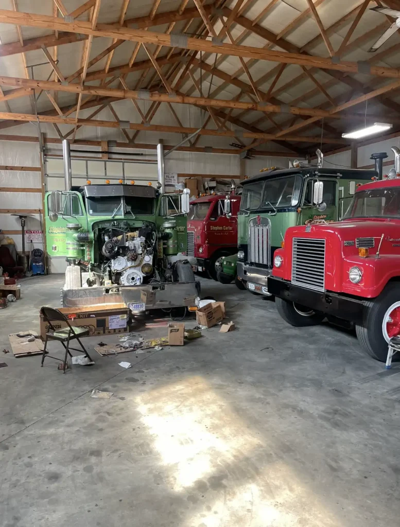 Several Diesel trucks in a garage with the engine exposed on one.